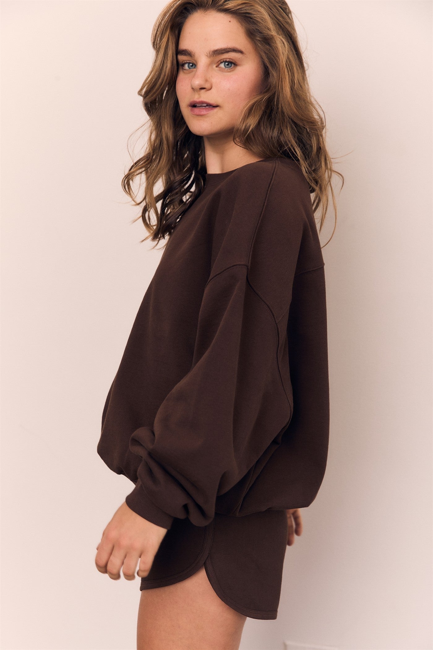 Woman wearing a brown oversized sweater against a plain background
